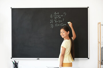 Cute little schoolgirl writing on blackboard in classroom