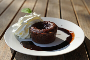 Tasty sweet chocolate souffle with warm sauce and cream on terrace garden table, popular modern desert served in many cafes