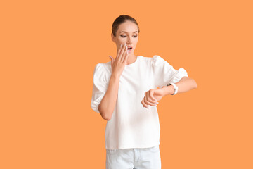 Shocked young woman with wristwatch on color background