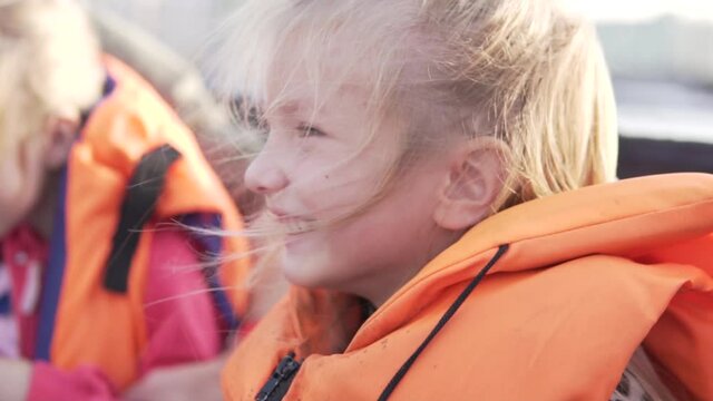 A happy little girl in a life jacket rides a motorboat on the river.