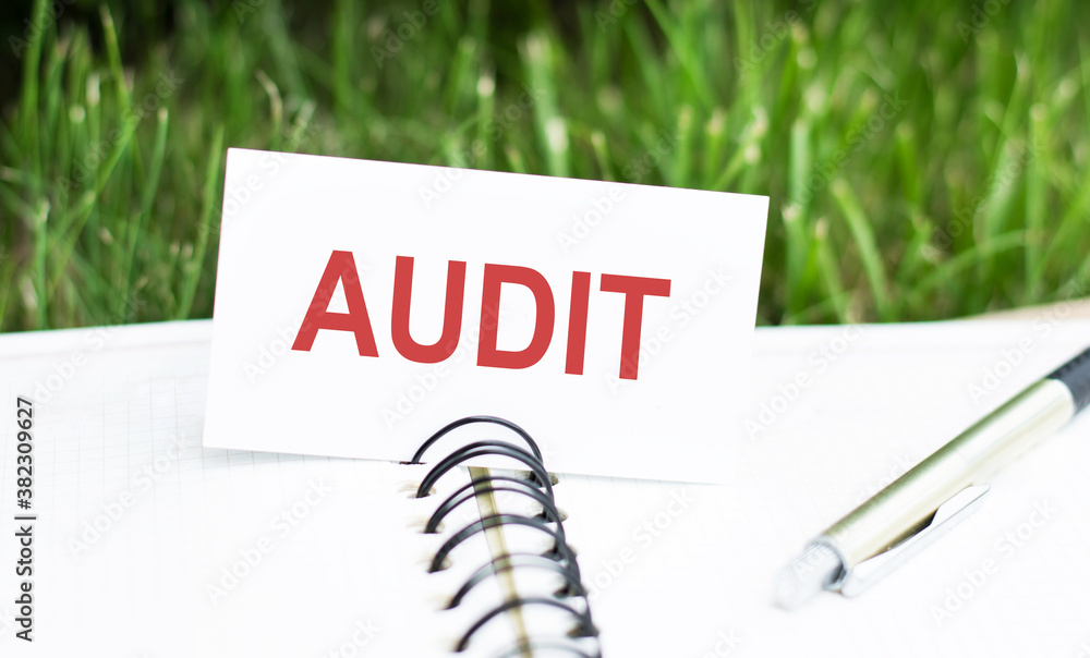Poster card with text audit on a notebook with a pen on a green background