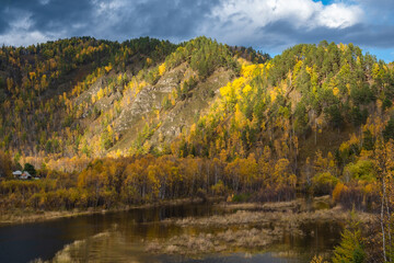 Picturesque autumn landscape with colorful bright forest. Countryside house. Dramatic stormy sky in the mountains.