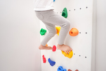 Close up of legs of little kindergarten boy having fun trying to climb on a small rock wall indoor...