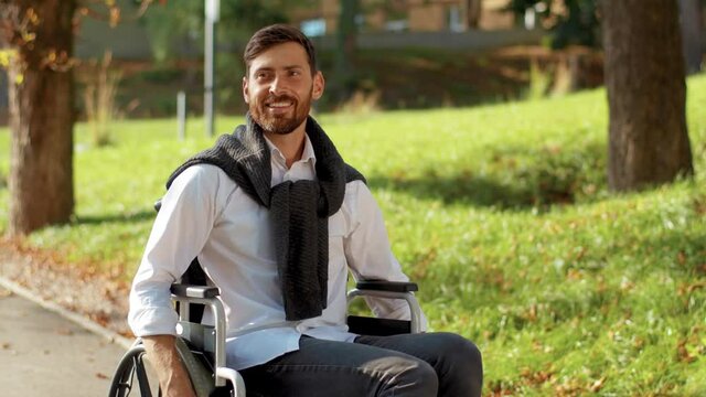 Portrait of happy handsome disabled man rides in wheelchair at sunlight smiling in park. Paralysis disability positive handicapped. Slow motion