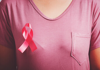 Breast cancer awareness healthcare and medicine concept. Close up Asian woman wear pink shirt standing with pink breast cancer awareness ribbon pin on chest, studio shot isolated on white background