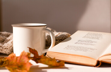 Cup and book on the table. Autumn yellow leaves and beige knitted blanket