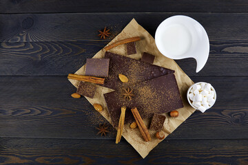 Ingredients for making hot chocolate. Chocolate, cocoa powder, cinnamon, anise star, marshmallow, and milk on rustic wooden background. Top view, copy space.