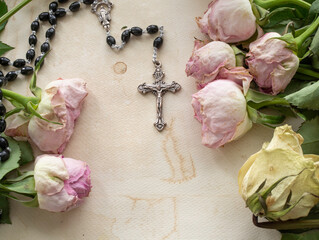 Rosary on an stained paper surrounded by dry pink and white roses, closeup with selective focus and copy space