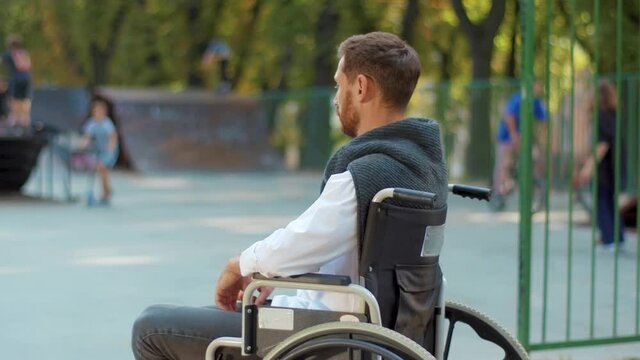 Shot back depressed man sitting on a wheelchair look at playground in park feel sad. Paralyzed disease health care desperation impairment. Slow motion