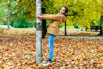 A cute happy girl stands by a birch tree in a city autumn park.