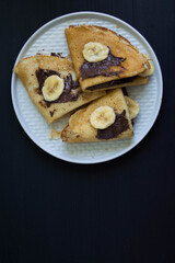 Crepes with nutella and sliced banana on the black background