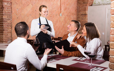 attentive woman waiter receiving order from guests in country restaurant