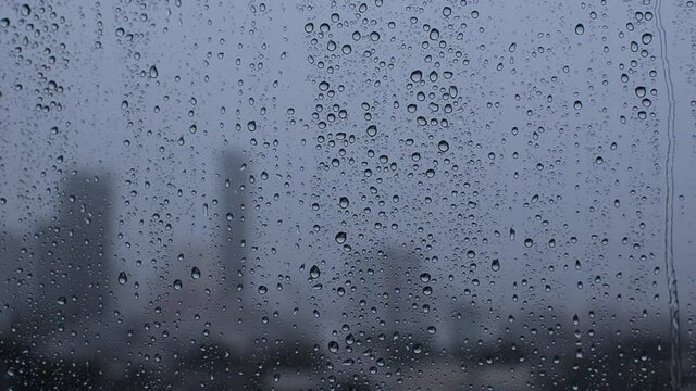 Footage of rain drop on glass window with blurred city background.