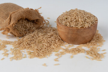 Brown rice in a sack and a wooden bowl overflowing out and scattered on the floor.