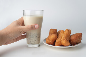 Hand holding glass of soy milk and chinese doughnut sticks on dish on white background.