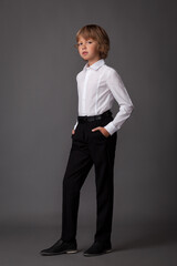 Handsome child guy blond sholnik in a white shirt and black pants on a gray background