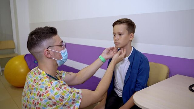 The doctor touches neck of the boy. Checking tonsils at pediatrician. Boy at kids clinic.