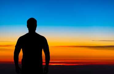 Silhouette of a man, back side, standing in front of beautiful sky during sunset