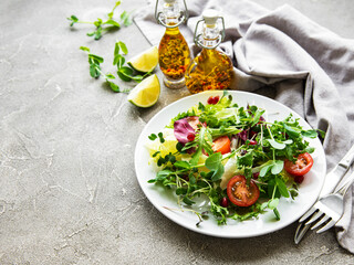 Fresh green mixed  salad bowl with tomatoes and microgreens  on  concrete background. Healthy food, top view.