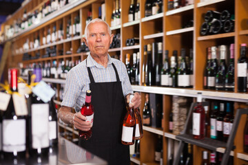 Nice male vintner working in modern wine shop, arranging wine bottles on racks. - obrazy, fototapety, plakaty