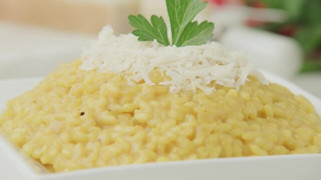 A Serving Of Creamy Risotto In A Plate Topped With Grated Parmesan Cheese And Parsley - Tilt Down Shot