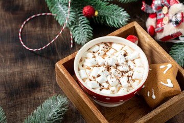 Cocoa with marshmallows in a red Cup and gingerbread on a tray on a Christmas background. Red decorations on spruce branches on a brown background	
