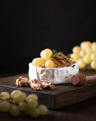 brie cheese with grapes and walnuts on a cutting board on wooden background, selective focus. 
