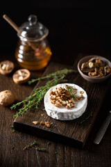 brie or camembert cheese with walnuts and honey on a wooden cutting board . Selective focus, dark...