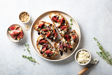 bruschetta with figs, cream cheese, balsamic sauce and pine nuts in a ceramic plate on a light background, top view