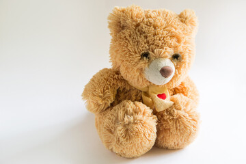 Soft Teddy bear with long light brown fur and a red heart on a scarf around his neck. Valentine's day gift, children's toy. White background, space for text