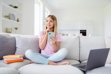 Full size photo of minded smart kid girl sit comfort couch legs crossed rest relax use smartphone think thoughts decide what post in house indoors homeschool