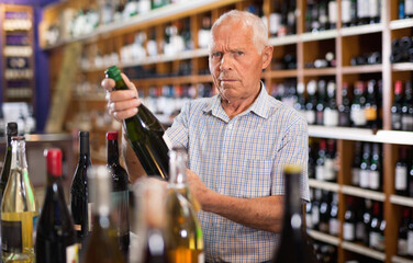 Happy cheerful grey-haired elderly man choosing wine in modern wineshop
