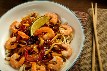 Close-up of udon with vegetables, mushrooms and shrimps near sticks.