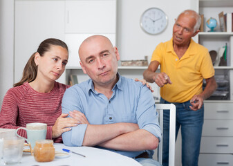 Unhappy family couple hugging after conflict, worried elderly man on backgroud