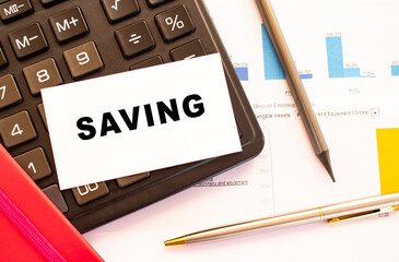 Text SAVING on white card with metal pen, calculator and financial charts. Financial concept.