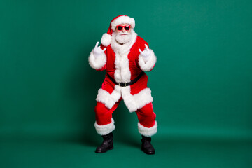 Full length body size view of his he nice attractive handsome bearded cheery cool Santa father having fun dancing showing double horn symbol isolated over green color background