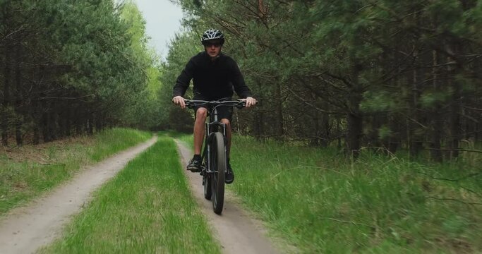 Young  man cyclist rides on a forest road. Teenager on a mountain bike rides through the forest. Man in a Bicycle helmet rides an mtb bike.