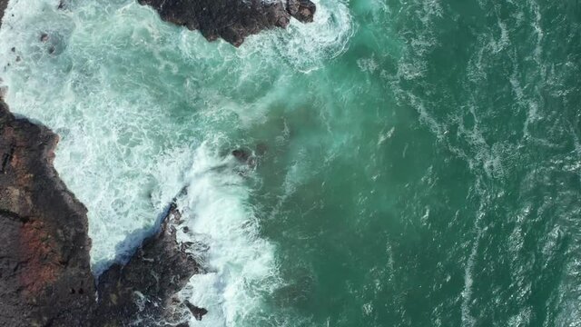 Rough shorebreak no swimming beach or coastline in Hawaii. Big waves rolling in rocky bay with black coral lava rock and stones. Overhead slow motion drone shot sunny day. Rip current dangerous spot