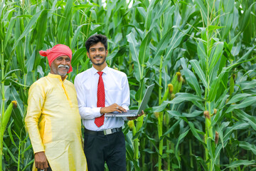 Indian farmer with agronomist at corn field and showing some information in laptop