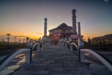 Fototapeta na wymiar Sunrise of the mosque with dramatic sky. Mosque with flower garden and bridge over the pool. 