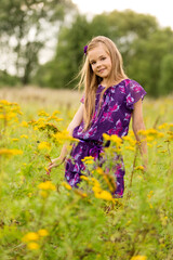 Naklejka na ściany i meble Beautiful blonde girl child in a bright dress outdoors in the tall grass