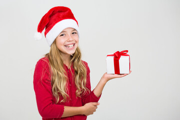 Cute smiling girl in red dress and santa hat giving gift box with red ribbon isolated on white background, child giving Christmas present, banner copy space. Isolated on white background.