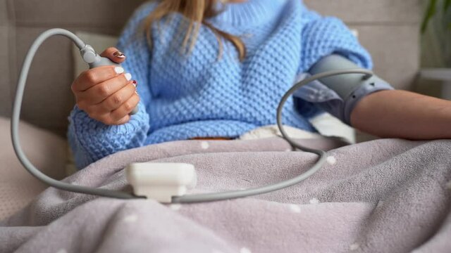 Woman measure blood pressure with medical device at home staying in bed.