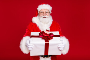 Portrait of his he nice handsome attractive cheerful overweight glad bearded Santa father holding in hands big large white giftbox celebrate isolated bright vivid shine vibrant red color background