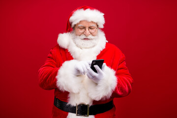 Portrait of his he nice attractive handsome cheerful focused Santa father using device gadget 5g web service blog post smm comment isolated over bright vivid shine vibrant red color background