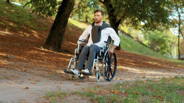 On sunny day young man disabled in wheelchair rides in park at sunlight. Paralysis disability handicapped. Serious. Autumn outside. Slow motion