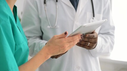 Closeup view of man and woman doctors using tablet during working day at clinic spbas. African American person and his female colleagues use electronic device and work together while standing indoors