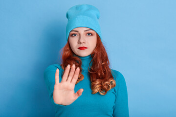 Confident redhead woman keeps palms towards camera, has displeased expression, looks at camera,...