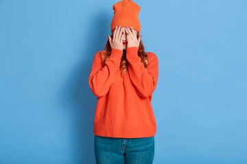 Joyful woman covers eye with palms, tries to hide from someone, adorable female wears sweater, cap...