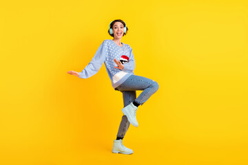 Full body profile photo of attractive crazy lady party newyear discotheque listen cool earphones dance floor night club wear ugly ornament sweater jeans shoes isolated yellow color background - obrazy, fototapety, plakaty